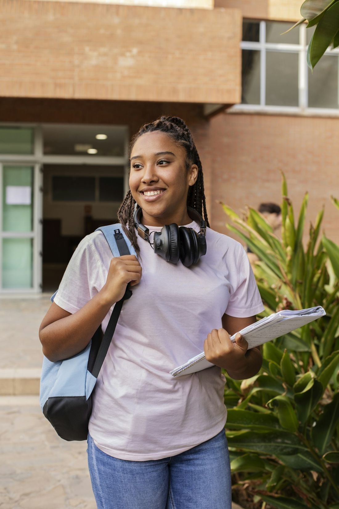 Étudiante souriante avec son sac à dos et ses cahiers sur un campus
